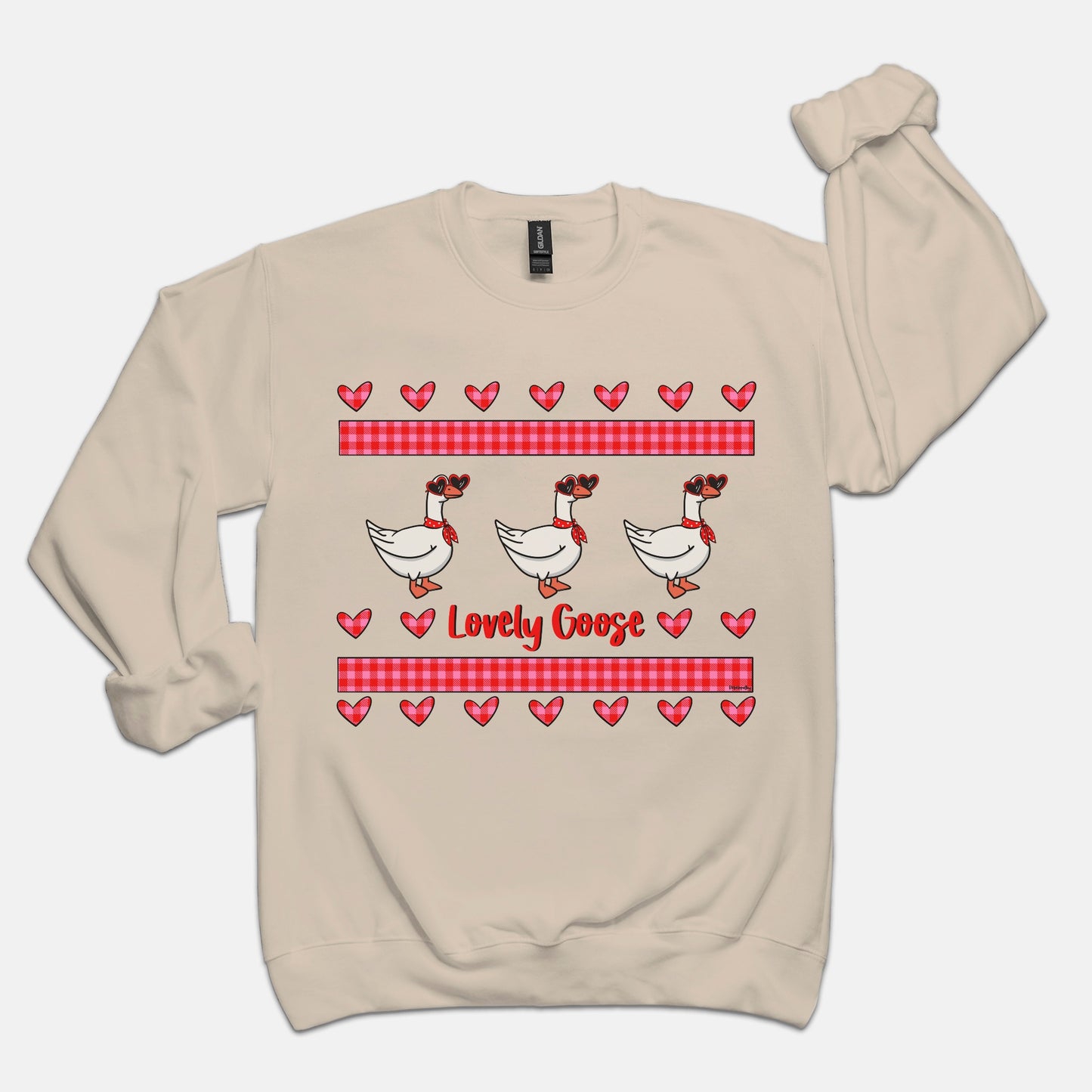 Porch goose cream/beige sweatshirt featuring three porch geese in heart shaped sunglasses and red cloth tied around the neck with plaid pink and red rectangles above and below and several hearts creating a love design. Text reads, “Lovely Goose”. Plain white background.