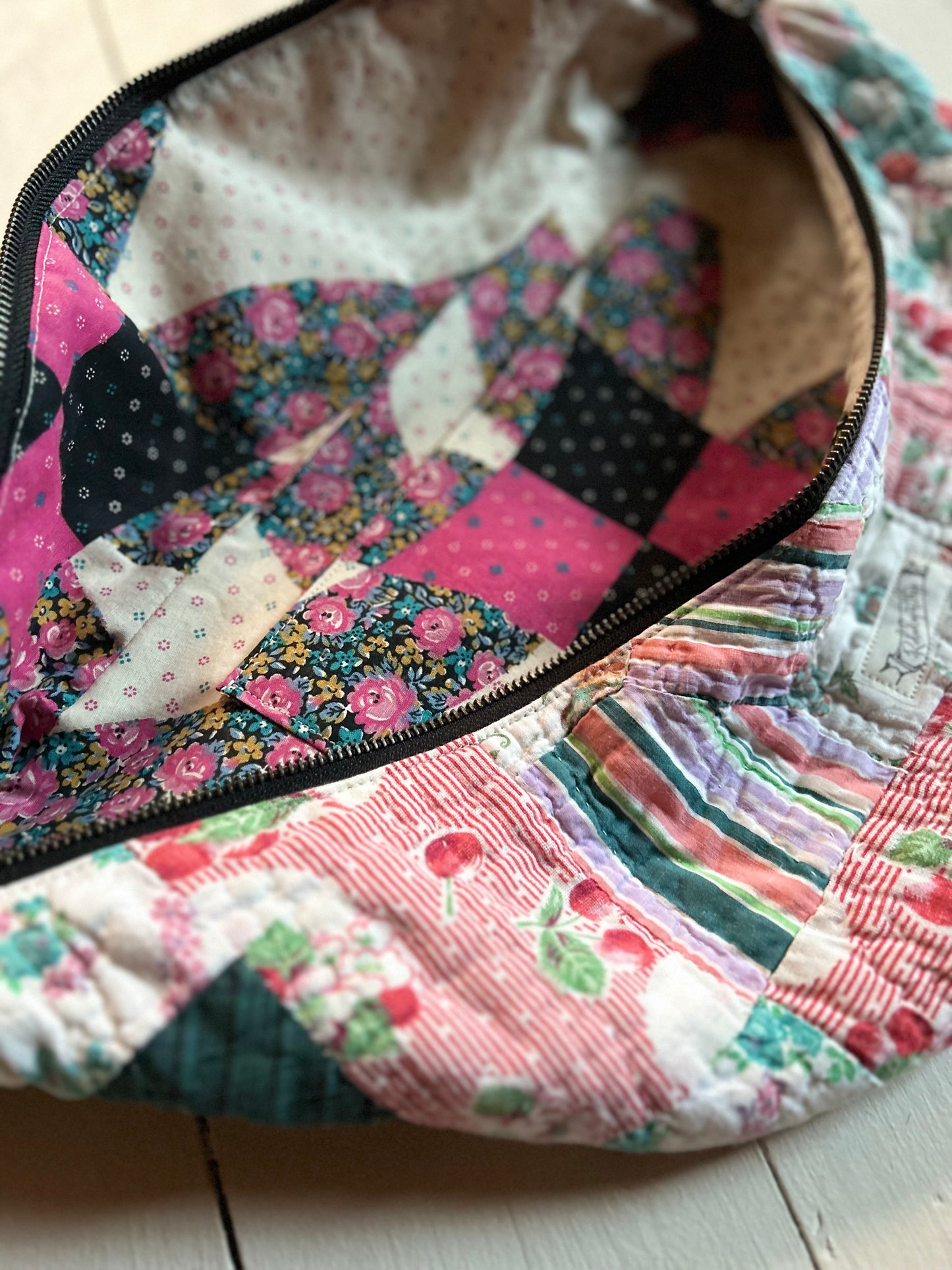 Close-up of a colorful quilt with cherry patchwork pattern sling bag on a wooden surface.