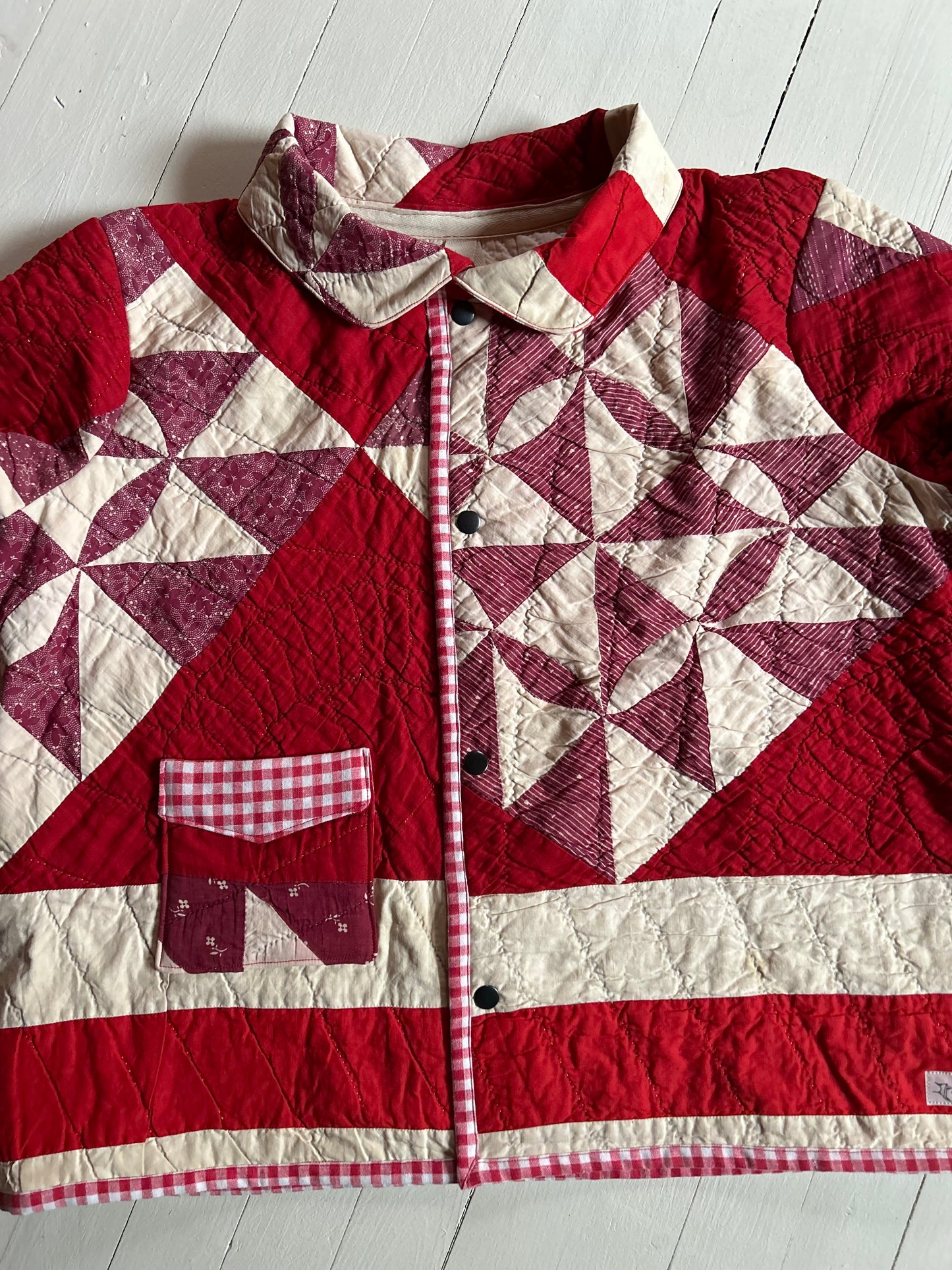 Vintage Quilted handmade jacket with red and white pattern on a light wooden floor with buttons and one pocket. 