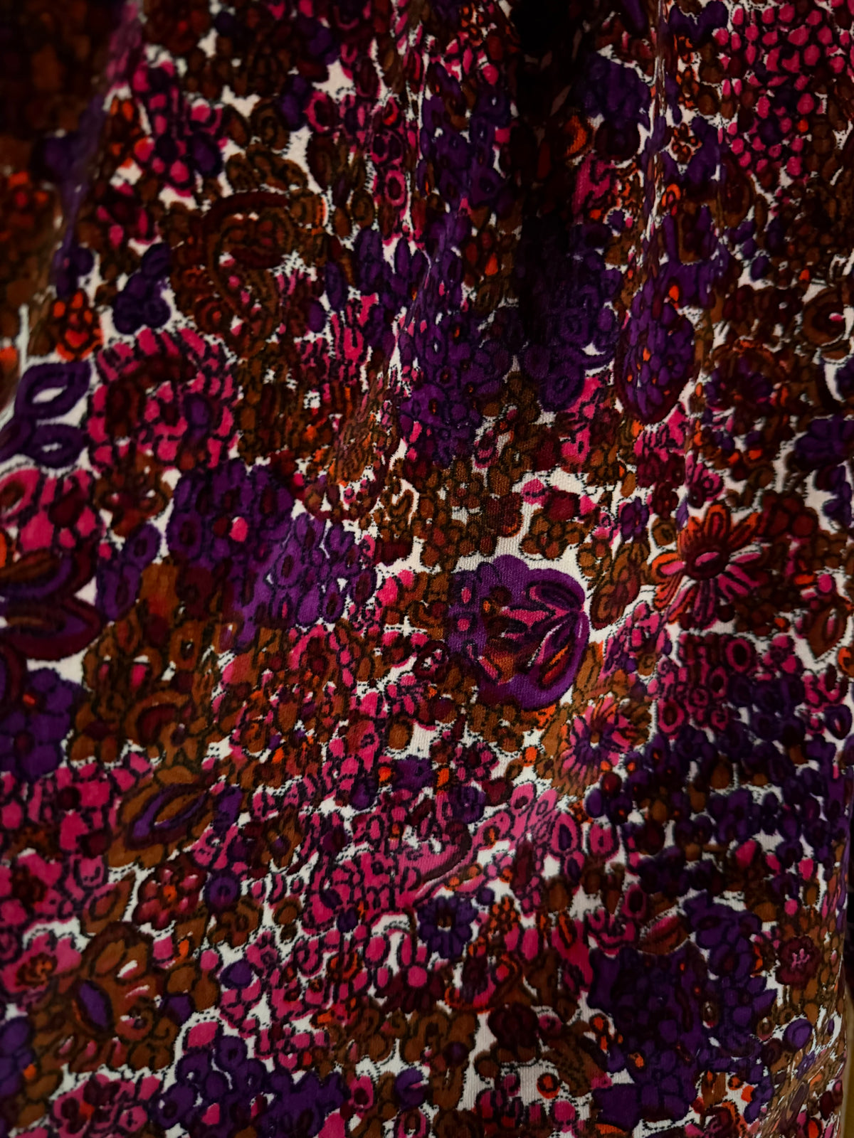 A close-up of a highly patterned velvet fabric featuring an abstract, dense floral and paisley-like print in deep purple, magenta pink, brown, and white.