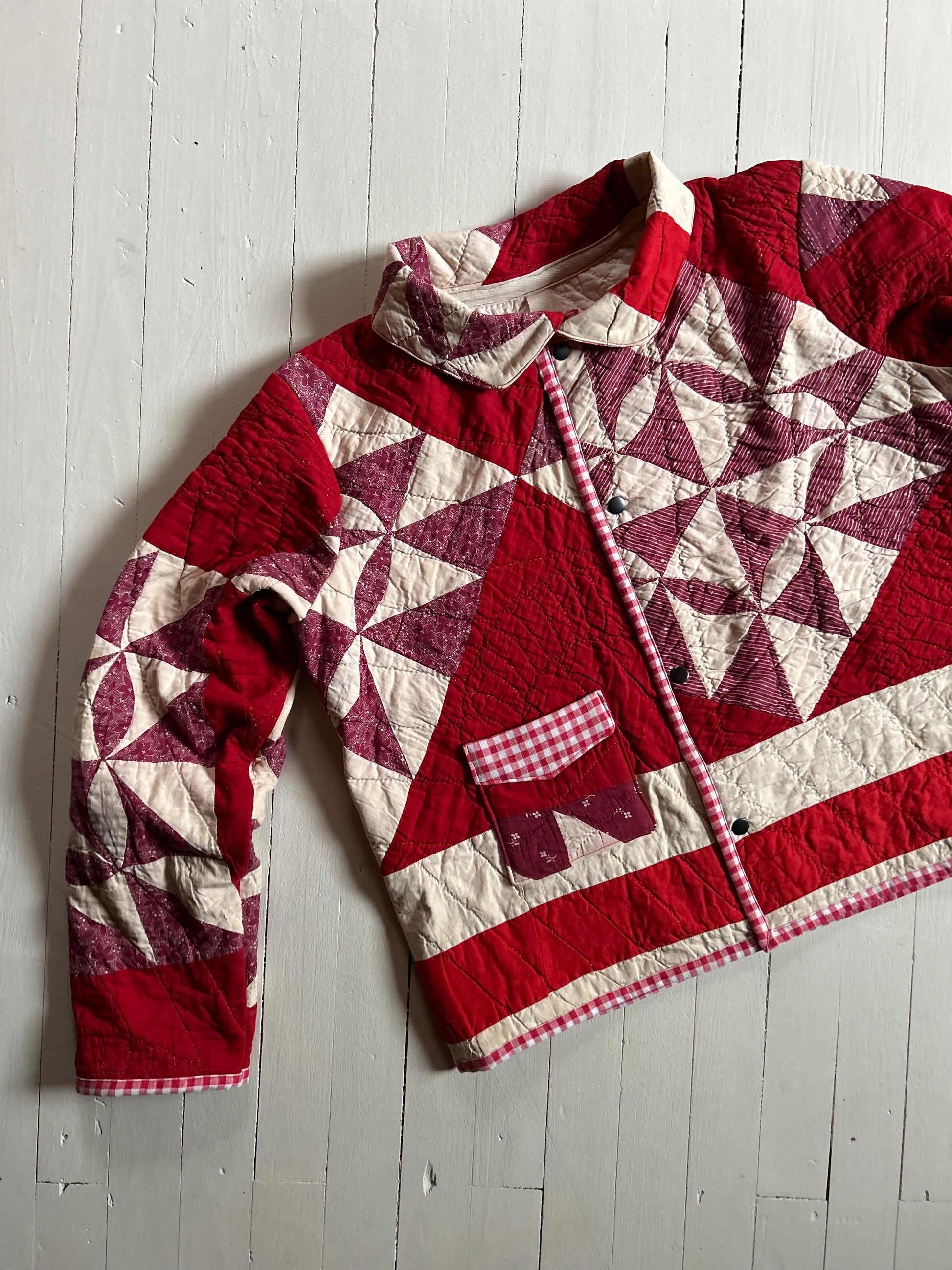 Vintage Quilted handmade jacket with red and white pattern on a light wooden floor with buttons and one pocket. 