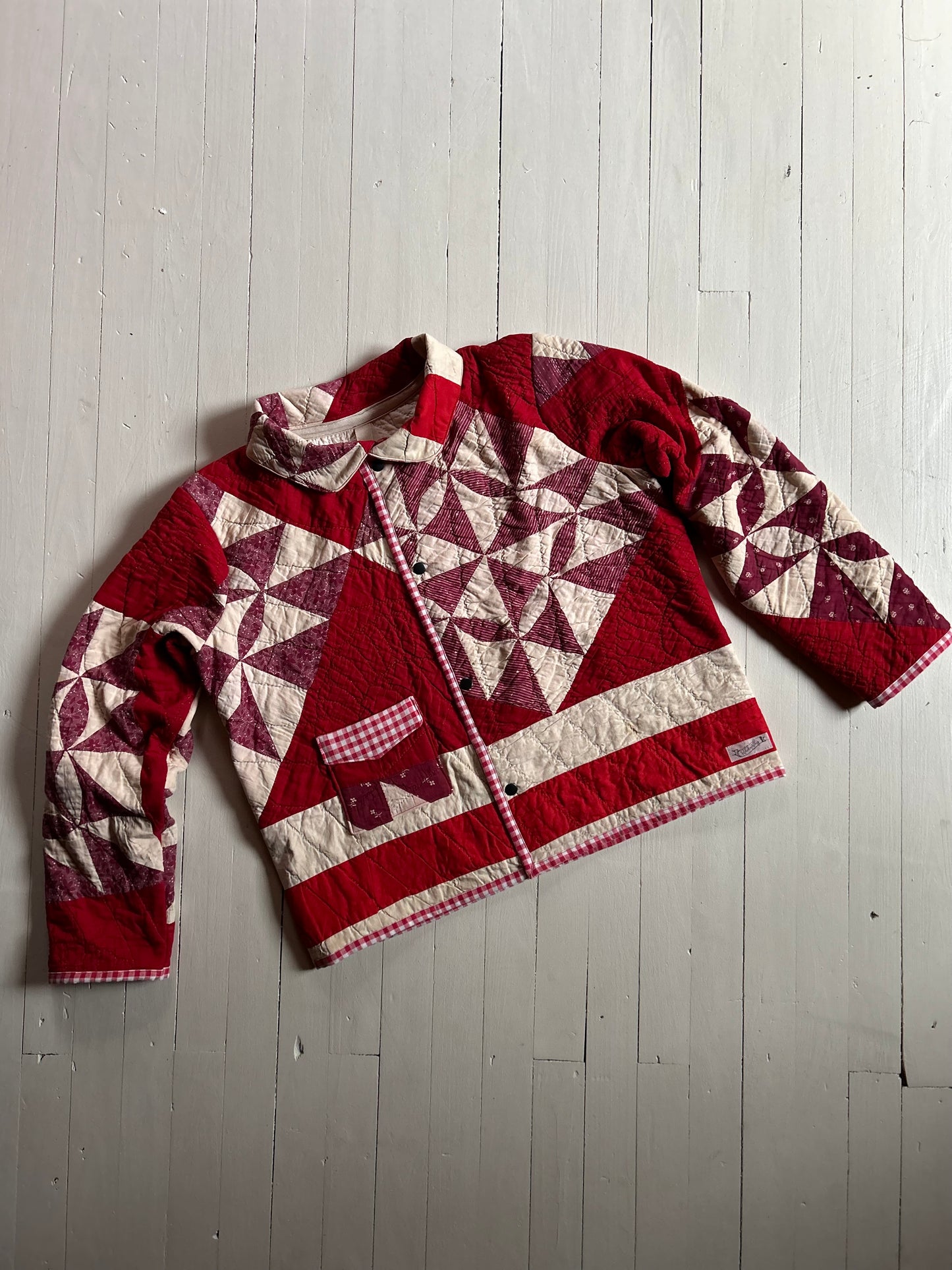 Vintage Quilted handmade jacket with red and white pattern on a light wooden floor with buttons and one pocket. 