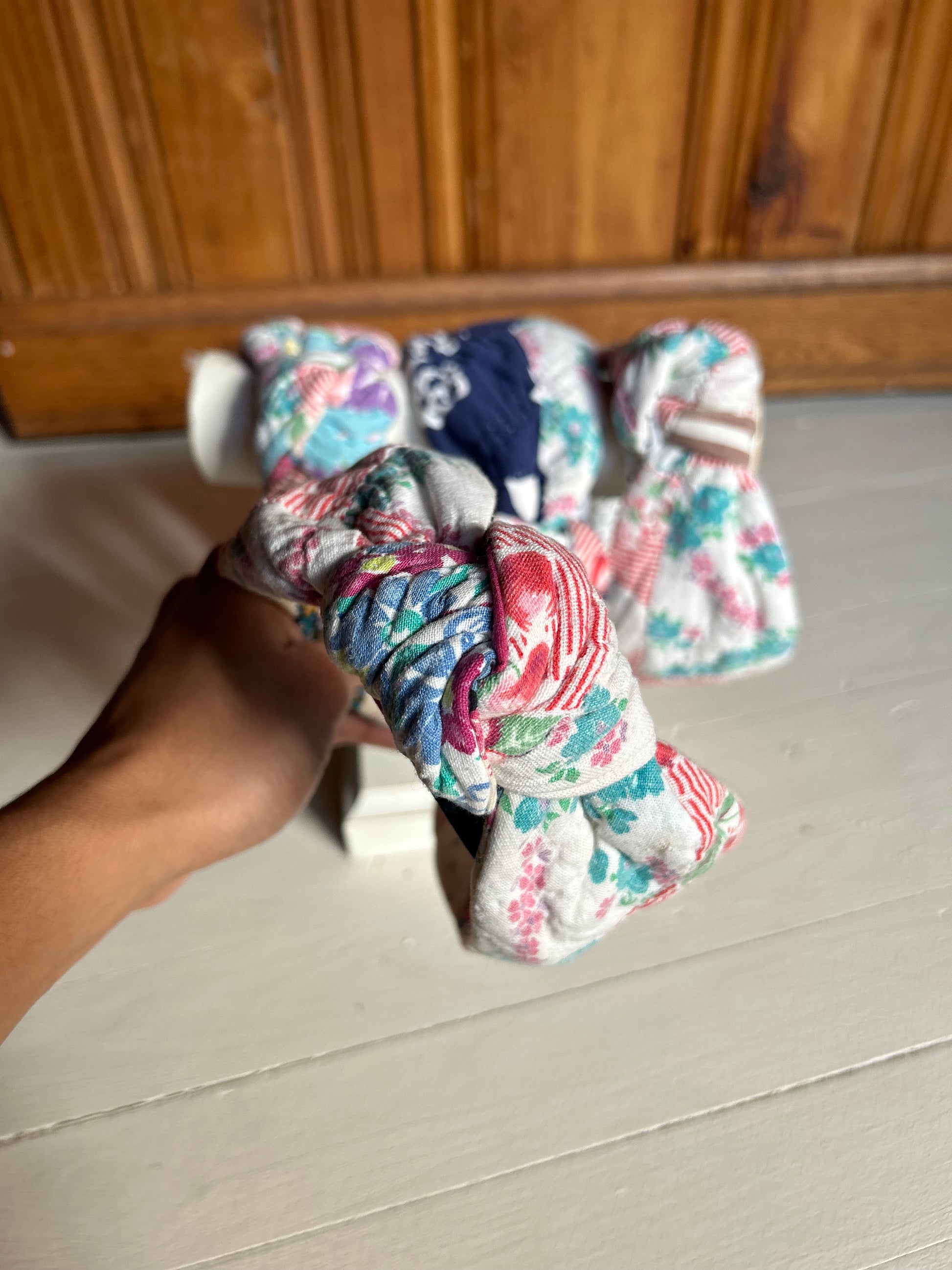 Hand holding floral-patterned knotted vintage quilt headbands over a wooden floor.