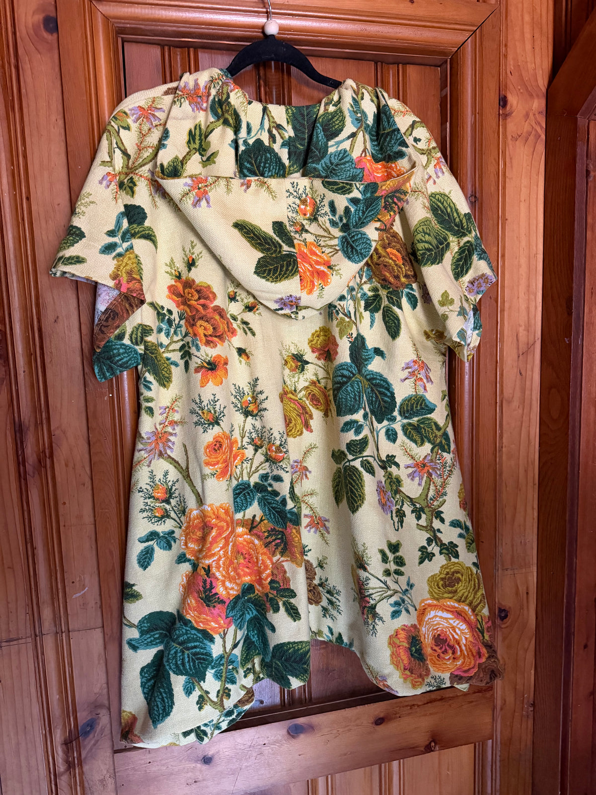 A short-sleeve blouse with a vintage floral print hanging on a black hanger against a wooden door background.
