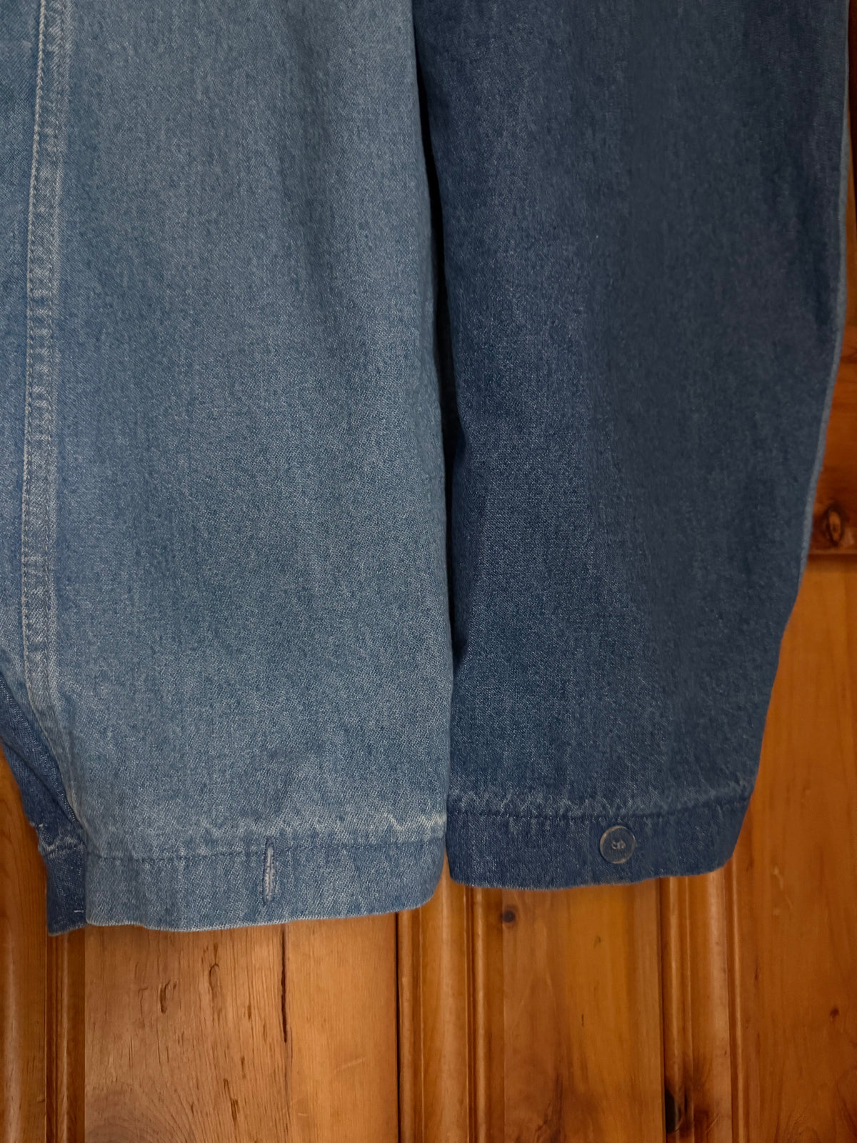 Close-up of blue denim shorts or capri pants hanging against a wooden door, showing the fabric texture and hem detail.