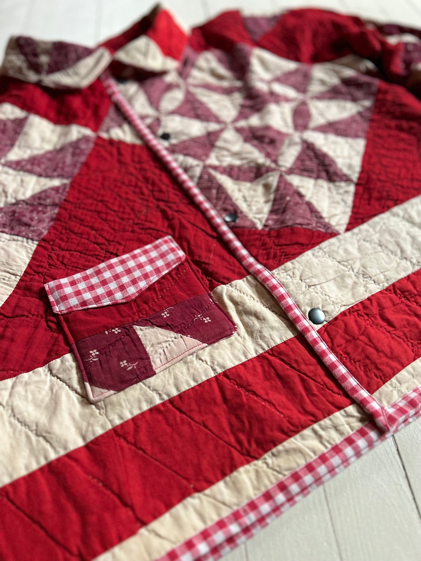 Close up of Vintage Quilted handmade jacket with red and white pattern on a light wooden floor with buttons and one pocket. 