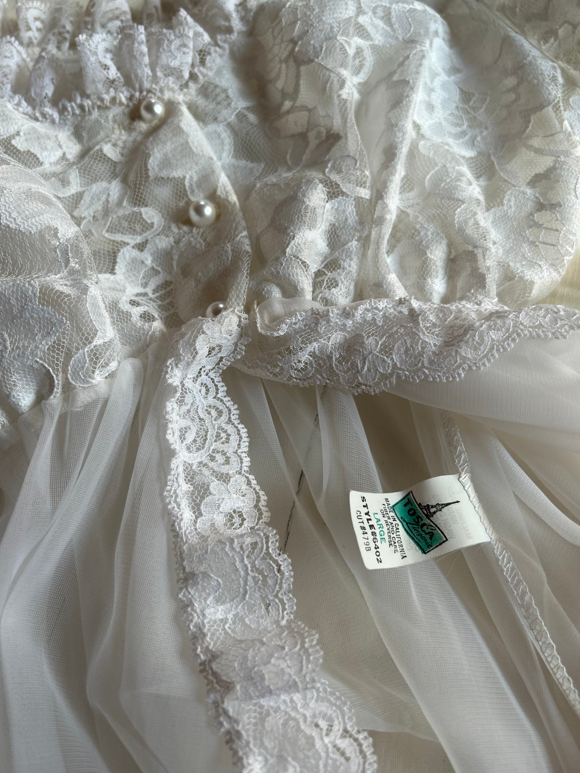 Close-up of a white lace garment with a tag, possibly a wedding dress or bridal gown.
