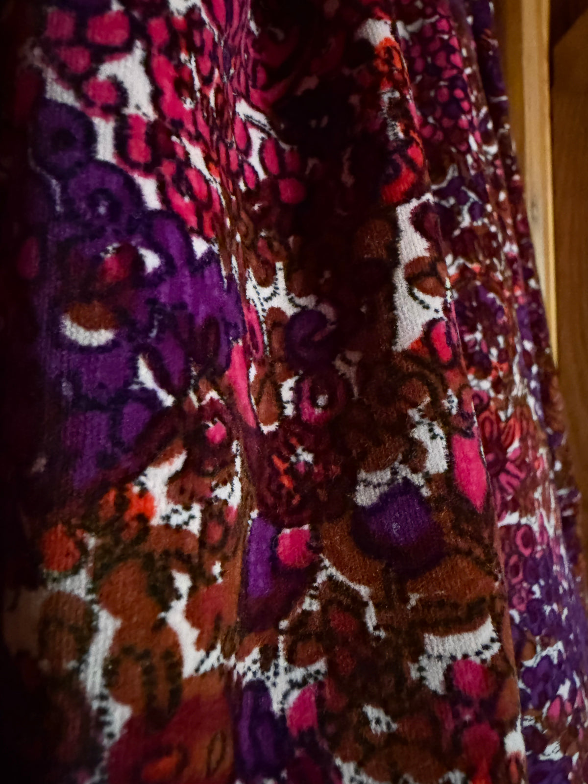A close-up of a textured velvet fabric with an intricate floral and paisley pattern in deep purple, magenta, brown, and white.