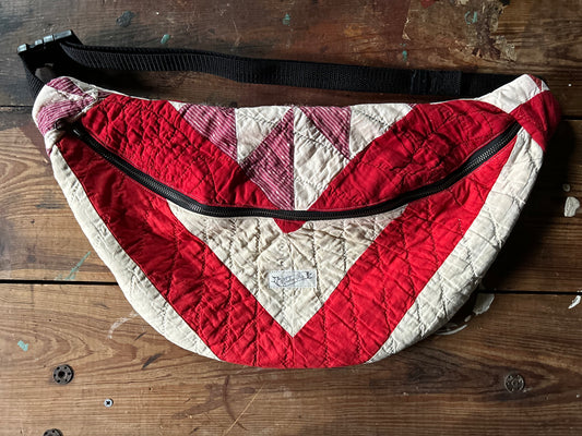 Vintage Quilt in red and white constructed into a crossbody bag with a black nylon strap, gun metal black metal zipper on a wooden surface.