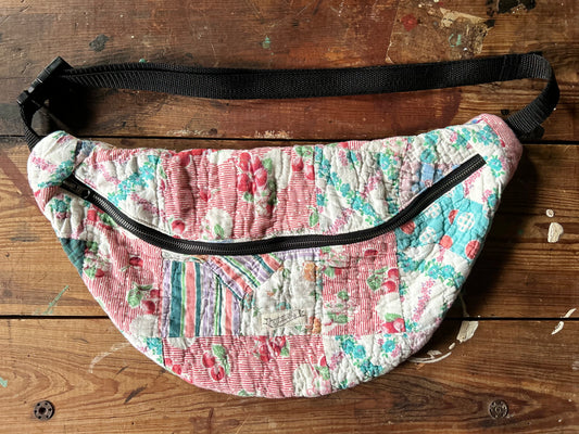 Photo of an oversized colorful quilt zipper sling bag with black adjustable strap, floral patterns with cherries hanging on a wooden door.