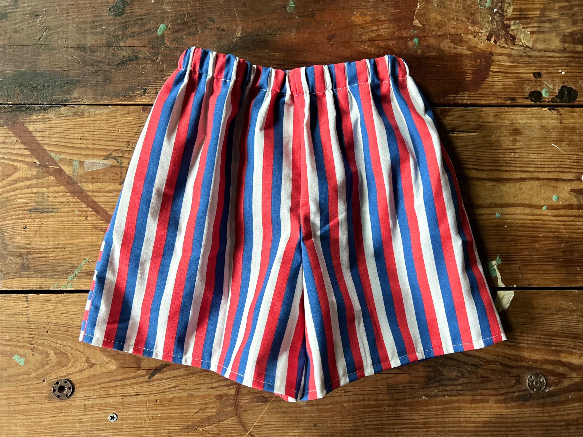 Back view of Pair of children’s red, white and blue shorts. Featuring a red, white and blue stripe in a vertical stripe.