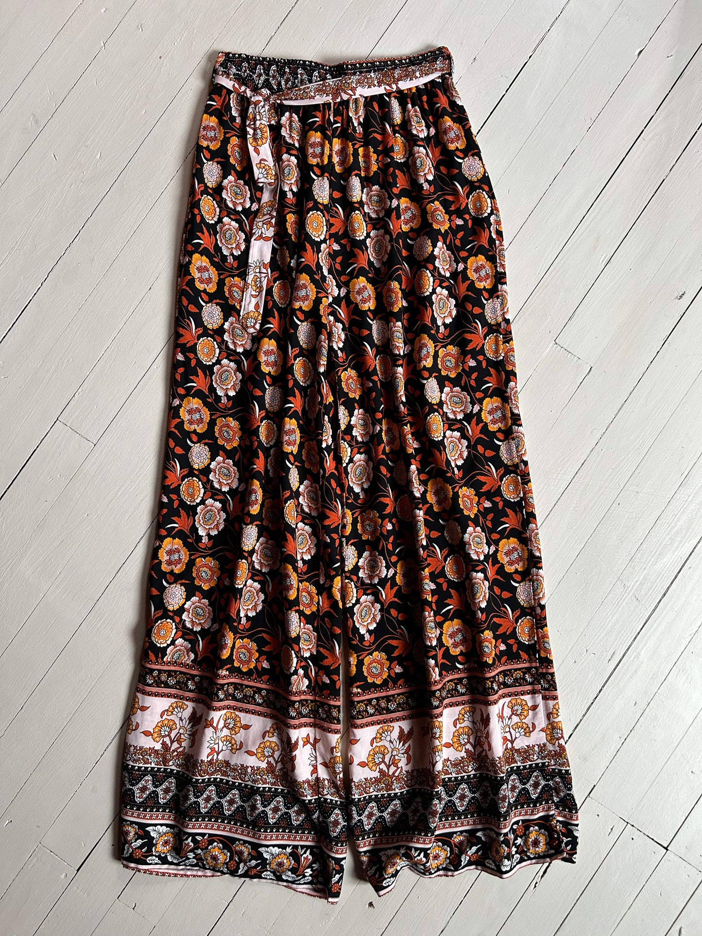 White wooded background. Black elastic pants with orange and white floral. 