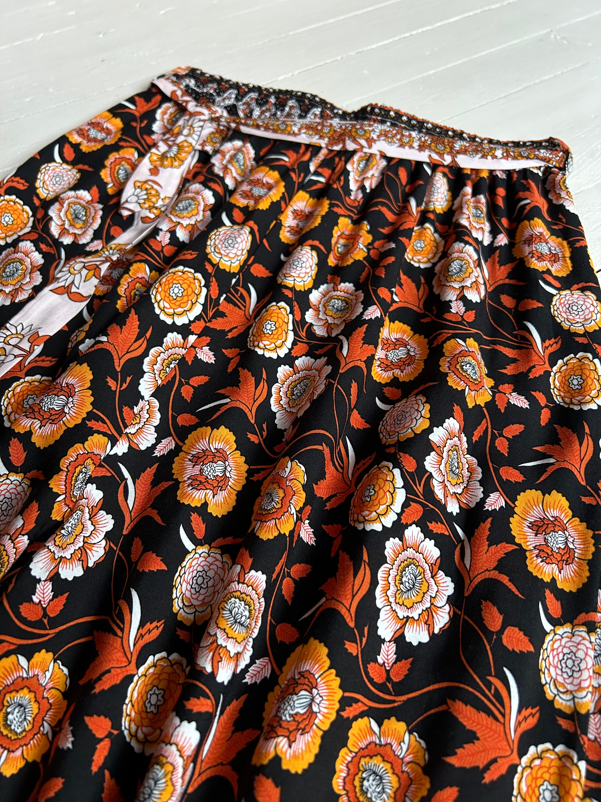 White wooded background. Black elastic pants with orange and white floral . Closeup of front .