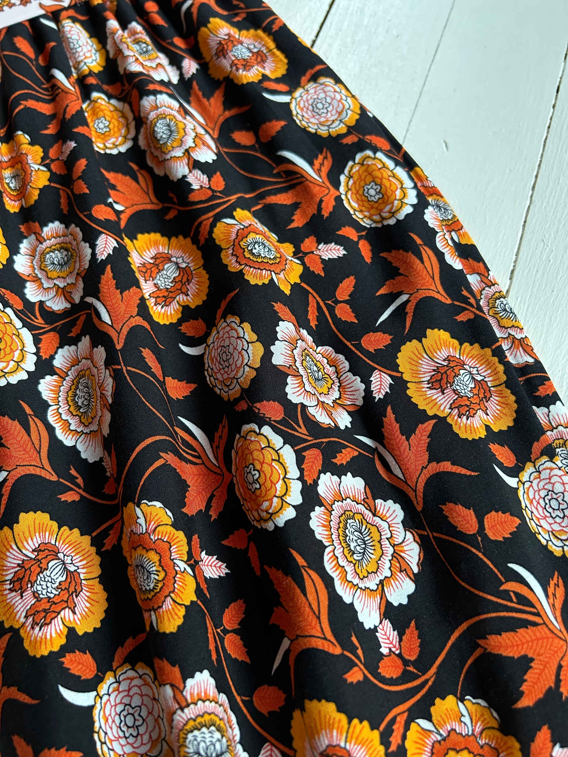 White wooded background. Black elastic pants with orange and white floral . Closeup of the floral and fabric.